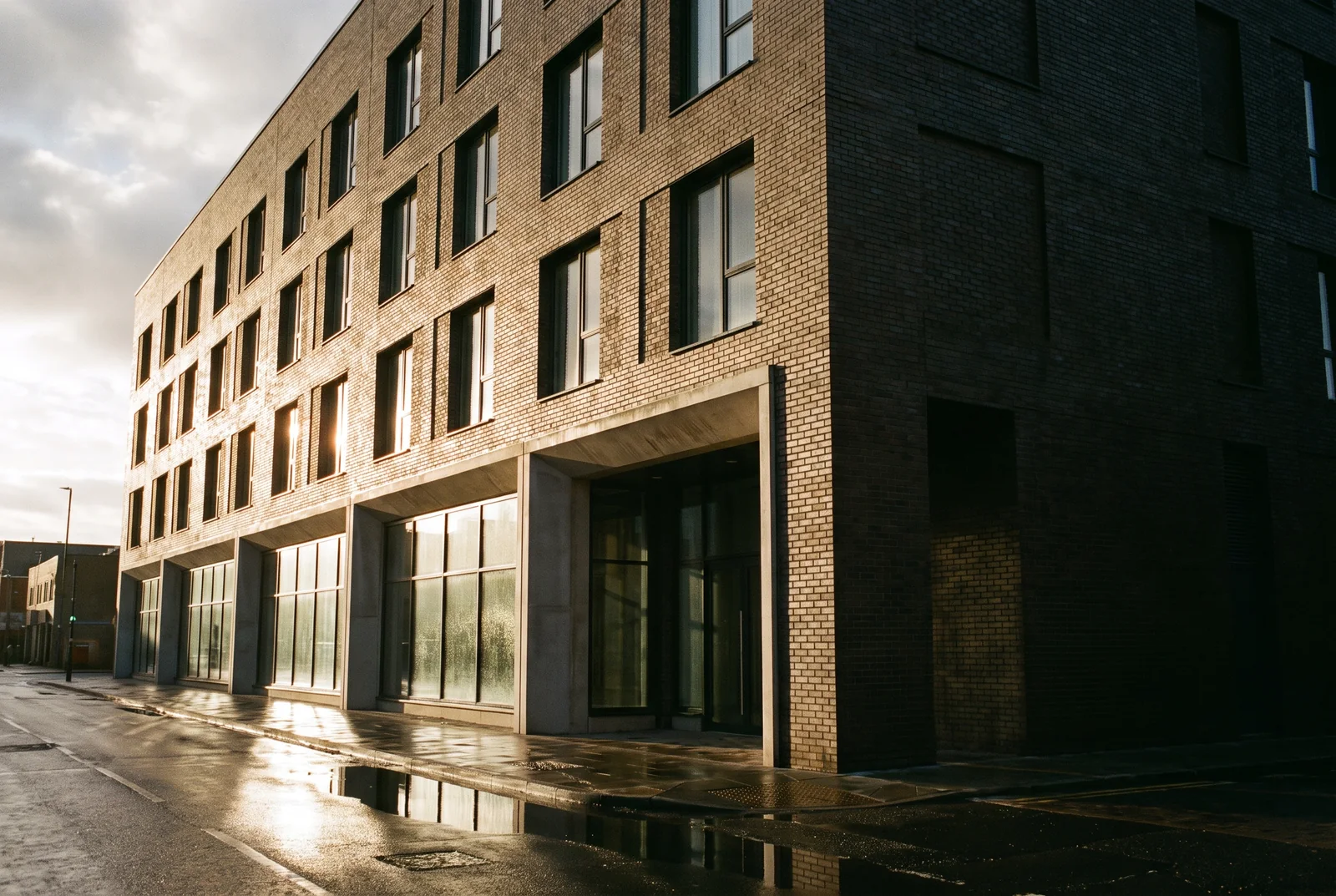 A five-storey mixed-use building with dark brick upper floors and a glazed ground floor, hard winter sunlight raking across the brick.